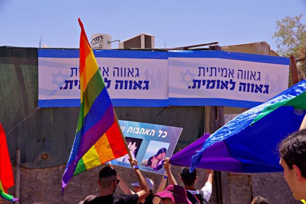 דגלי גאווה במצעד, כשברקע שלטים שנתלו ברחוב נגד הקהילה הלהט"בית (צילום: ארז וולך)