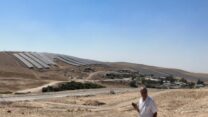 סלמאן אל-ע'נאמי בשכונה החדשה באבו קרינאת, על רקע השדה הסולרי (צילום: באסל אלע'נאמי)