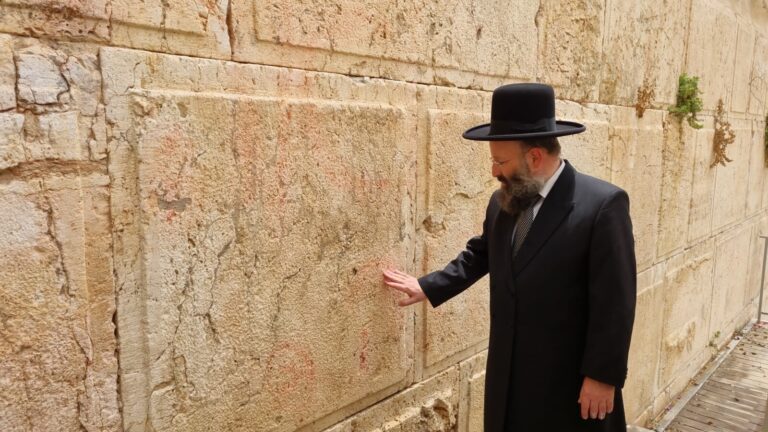 רב הכותל המערבי והמקומות הקדושים, הרב שמואל רבינוביץ', לצד קיר הכותל עליו רוססה כתובת המחאה נגד המלחמה (צילום: הקרן למורשת הכותל המערבי)