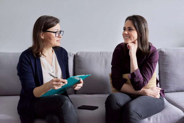Social worker, psychologist talking to young woman in office. Women sitting on couch, counselor making notes, listening to patient. Psychology, mental health, social difficulties of young people