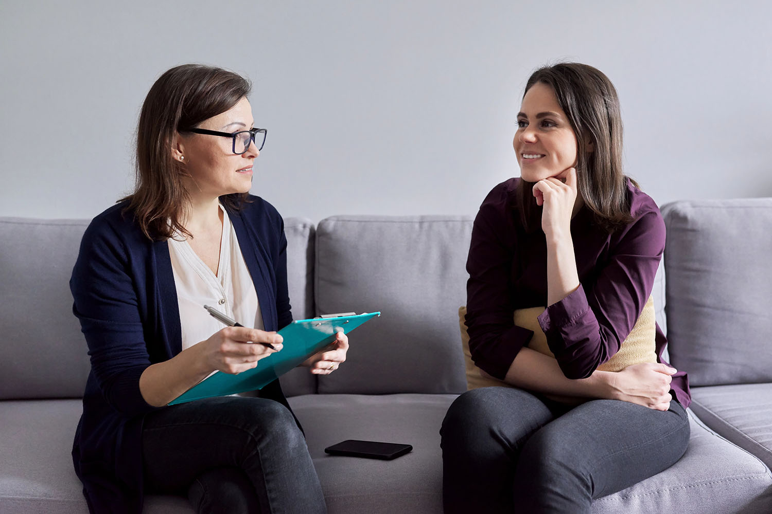 Social worker, psychologist talking to young woman in office. Women sitting on couch, counselor making notes, listening to patient. Psychology, mental health, social difficulties of young people