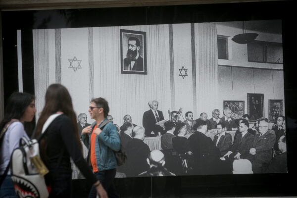 אנשים חולפים על פני תמונה של הכרזת העצמאות (צילום: מירים אלסטר / פלאש 90)