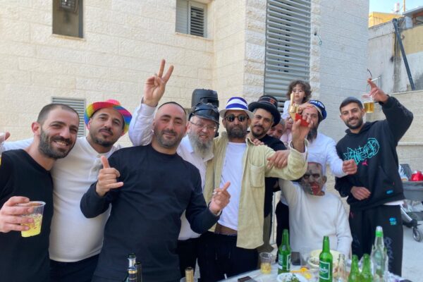 רב השכונה שנפגעה מטיל איראני בבית שמש, הרב יוסף עובדיה, עם תושבים החוגגים את פורים בזירת האסון (צילום: יהל פרג')