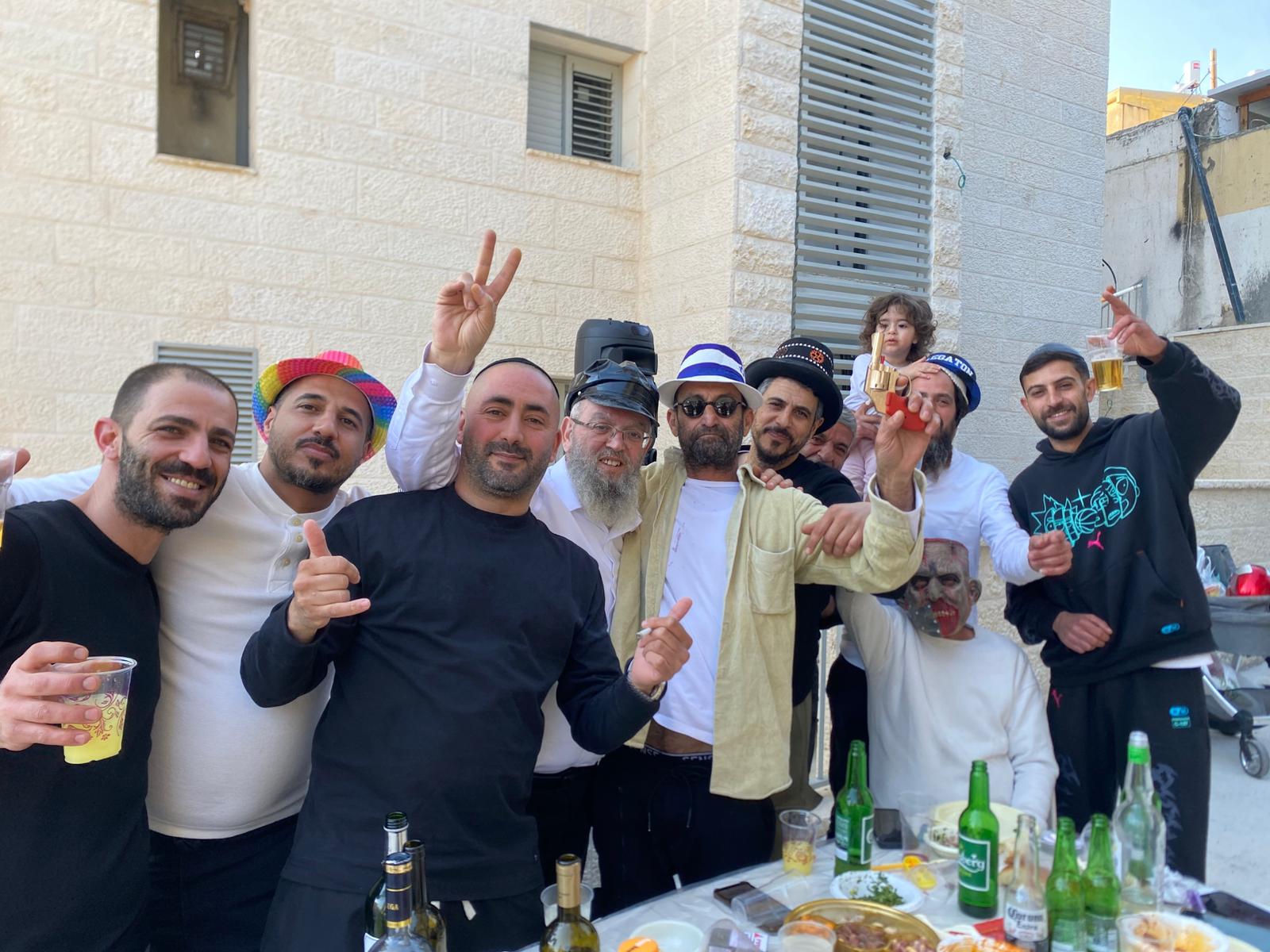 רב השכונה שנפגעה מטיל איראני בבית שמש, הרב יוסף עובדיה, עם תושבים החוגגים את פורים בזירת האסון (צילום: יהל פרג')