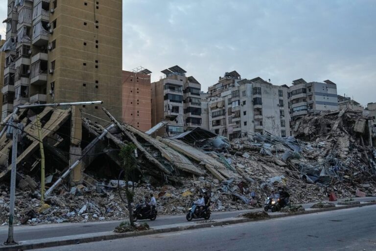 תושבים על רקע בתים הרוסים ברובע הדאחיה בביירות, בבוקר שלמחרת הפסקת האש בין ישראל ללבנון (צילום: AP Photo/Bilal Hussein)