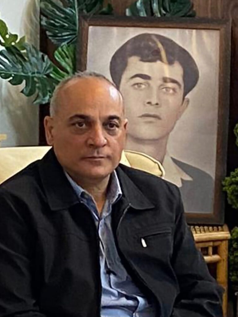 ווליד מולא ומאחוריות תמונתו של אביו רשיד ז"ל (צילום: אלבום פרטי)