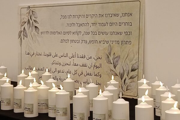 שולחן נרות זיכרון בכניסה לטקס, הנושאים את שמות החללים בעברית ובערבית. ברקע הצהרת המשפחות השכולות: "בוחרים היום לעמוד יחד, להתאבל ולזכור" (צילום: יניב שרון)
