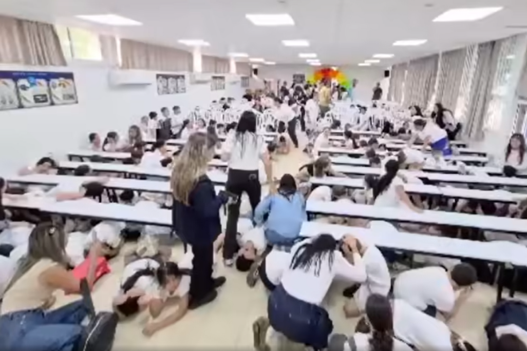 תלמידים בבית הספר 'מגינים' בקריית שמונה מתמגנים תחת שולחנות בעת אזעקה במהלך טקס שבועות (צילום מסך: רשתות חברתיות לפי סעיף 27א') תלמידים בבית הספר 'מגינים' בקריית שמונה מתמגנים תחת שולחנות בעת אזעקה במהלך טקס שבועות (צילום מסך: רשתות חברתיות לפי סעיף 27א')