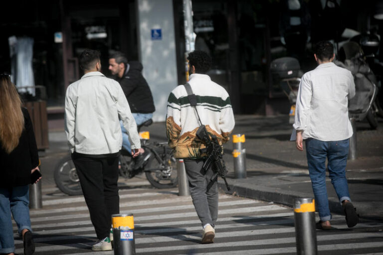 חייל מילואים בחופשה הולך עם נשקו ברחוב דיזנגוף בתל אביב. "לאחר שנות מלחמה – אנחנו מבקשים להפנות את המבט לצלקות ולכאבים של ילדים, נערים וגברים" (צילום: מרים אלסטר/פלאש90)