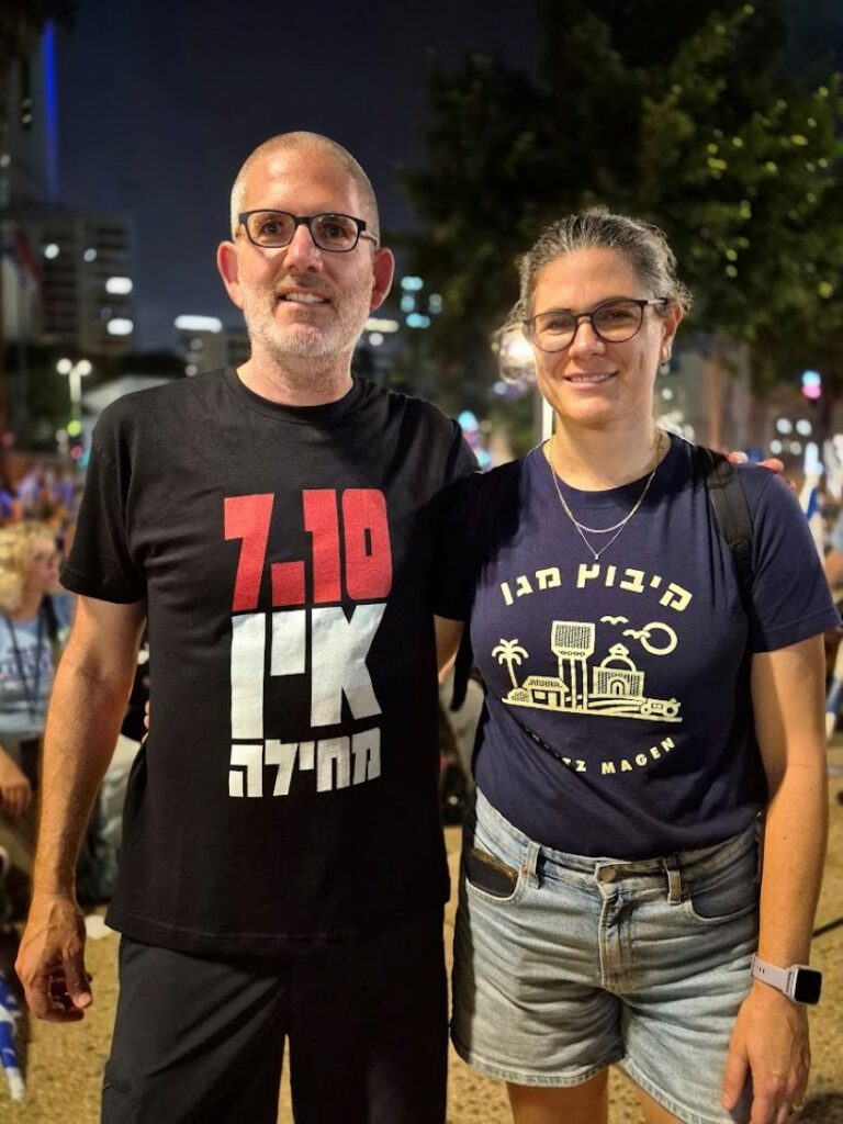 מפגינה עם חולצה של קיבוץ מגן בעוטף עזה לצד מפגין עם חולצת "7 באוקטובר אין מחילה" (צילום: יהל פרג')