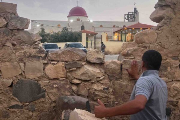גבר מביט דרך חרך בחומת אבן לעבר כנסייה יוונית אורתודוקסית שבה חמושים פתחו באש במהלך הלוויה שעות קודם לכן בכפר חמוד, במחוז כרק בירדן, יום שישי, 23 באוקטובר 2026 (צילום: AP)