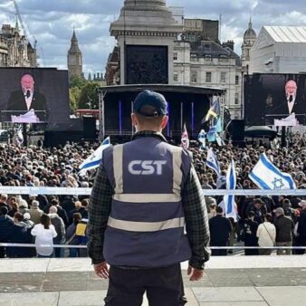 איש CST מאבטח עצרת של הקהילה היהודית בלונדון הצופה בדברי הרב הראשי של בריטניה אפרים מירוויס (צילום: CST)